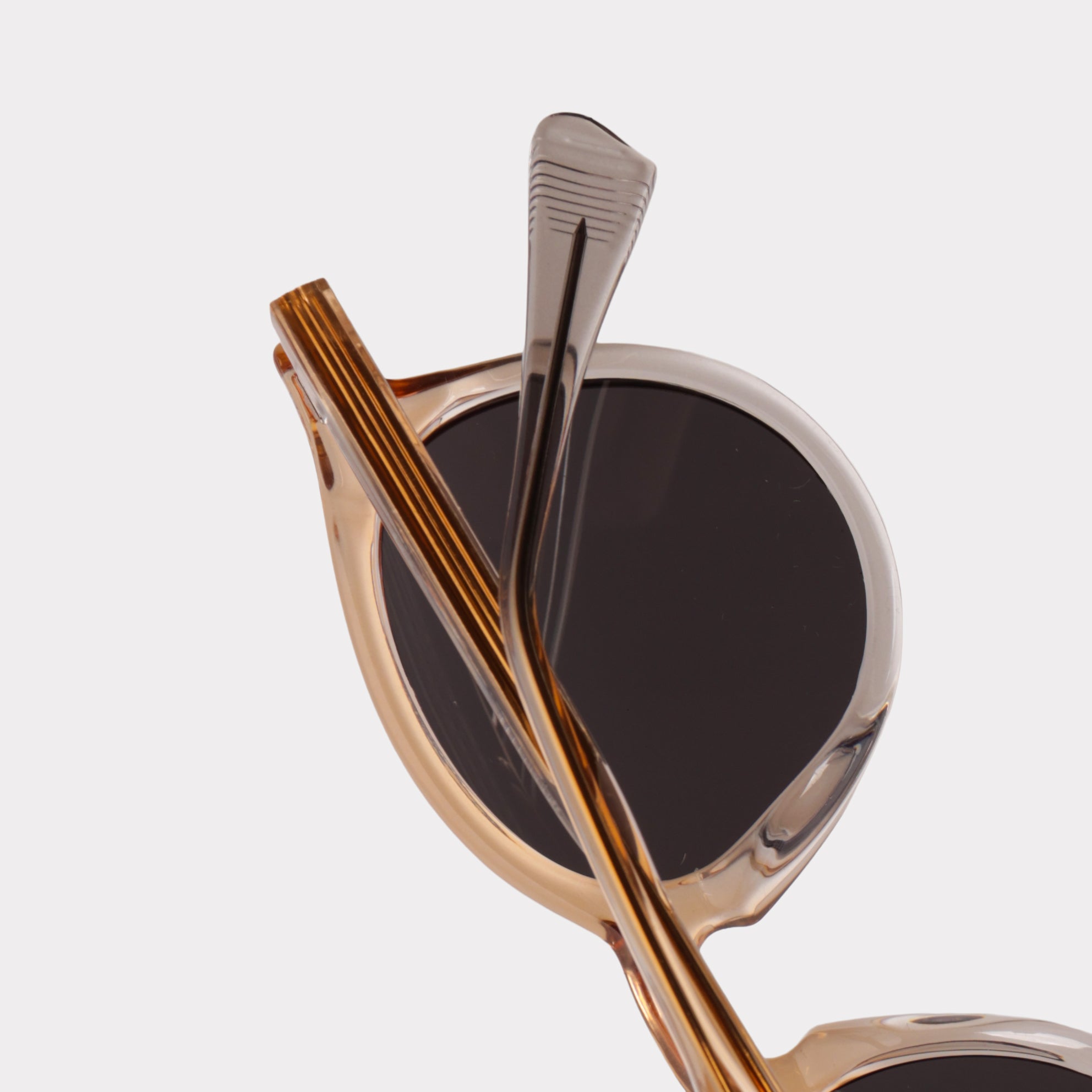 Close-up of a pair of sunglasses with gold frames and dark lenses on a light gray background